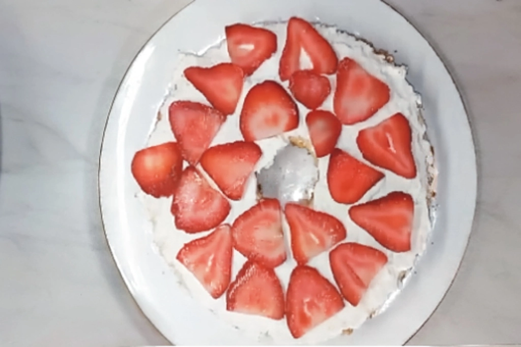 Whipped cream-covered cake topped with sliced strawberries